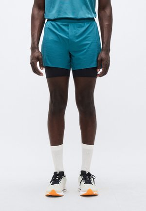 Sinakas akna elastse vöökohaga spordipüksid, kandes nende all musti kompressioonpükse. Komplektis valged soonikkoega sokid ja kerged jooksujalatsid.