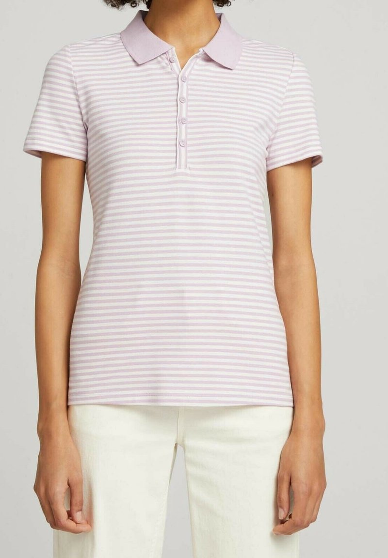 Femme portant un polo à manches courtes rayé horizontalement rose clair et blanc, associé à un pantalon écru.