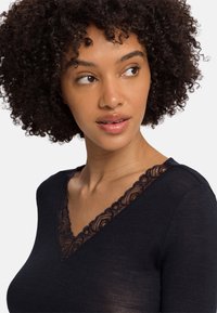 Top a coste navy con scollo a V e bordo in pizzo nero lungo il collo; texture morbida e design aderente.