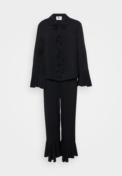 Fekete két részes öltözet, melyhez tartozik egy galléros blúz, nyakkendős részletek és harangujjak; hozzá illő nadrág harang szegéllyel. Sima anyag.