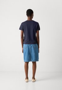 Tricou din bumbac navy cu mâneci scurte, asortat cu o fustă din denim bleu deschis, având o talie și buzunare pe spate. Pantofi slip-on bej.