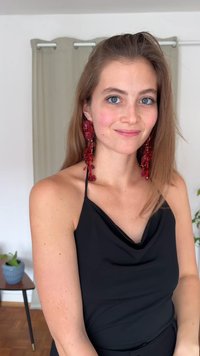 Röda lyktörhängen med blomsterdesign och pärlor, bärs med en svart ärmlös topp, mot en neutral bakgrund.