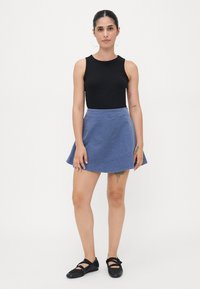 Svart ermeløs topp, lys blå denim A-linjert skjørt, flate svarte sko. Huden synlig, tatoveringer på armene. Enkelt design, tettsittende fasong.