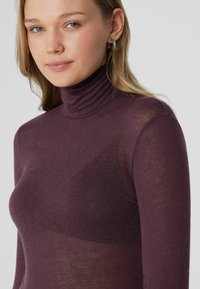 Fialový rolák vyrobený z lehkého, průhledného materiálu s žebrovanou texturou kolem límce, s úzkým střihem a dlouhými rukávy.