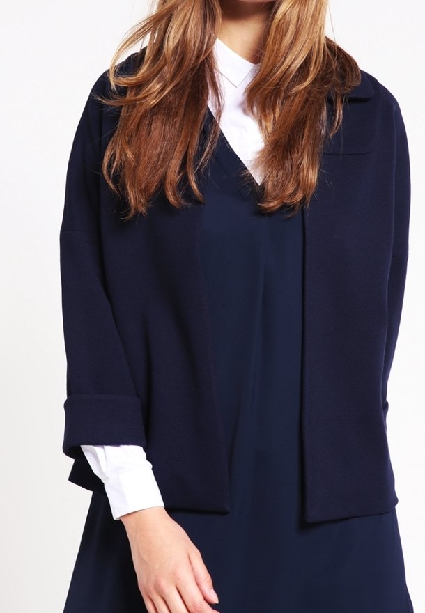 Žena v námořnickém modrém saku přes bílé košilové tričko, s dlouhými světlohnědými vlasy, které částečně zakrývají oblečení.