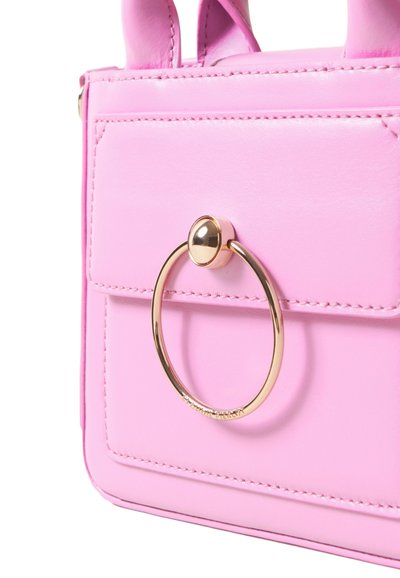 Dettaglio ravvicinato di una borsa in pelle rosa con una tasca frontale a pattina e un grande anello circolare dorato sulla tasca.