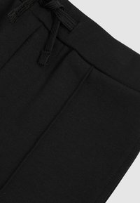 Zbliżenie na czarną talię dresów z sznurkiem i widocznym szwem na gładkiej tkaninie.