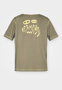 Camiseta verde oliva de manga corta, con texto gráfico amarillo y diseños en la parte posterior. Costuras en contraste a lo largo de los bordes.