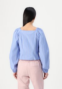 Blåstripete bluse med puffede ermer og firkantet utringning, kombinert med lys rosa bukser med elastisk midje. Glatt stoffstruktur.