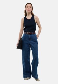 Débardeur côtelé bleu marine associé à un jean en denim bleu à taille haute et jambes larges, rehaussé d'une ceinture marron et d'un sac à main noir.
