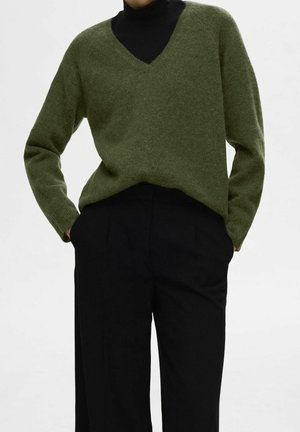 Pull vert à col en V fabriqué dans un matériau doux, avec des manches longues et une coupe légèrement ample, associé à un pantalon noir ajusté.