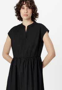 Black dress with short cap sleeves, a round neckline, and a gathered waistline. The fabric appears smooth and lightweight.