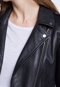 Zwarte leren motorjack met zilverkleurige hardware, asymmetrische rits en gestructureerde kraag. Draag het over een wit T-shirt met ronde hals.