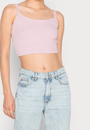 Crop top rose clair à fines bretelles, texture côtelée, associé à un jean en denim taille haute bleu clair.