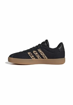 Zapatilla negra de corte bajo con suela de goma marrón y tres franjas con estampado de leopardo en el lateral sobre un fondo blanco.