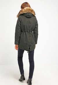 Parka verde scuro con colletto in pelliccia sintetica, vita regolabile con cordino e apertura sul retro con bottoni. Abbinata a jeans scuri e stivaletti.