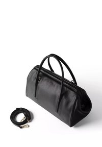 Sac à main en cuir noir avec deux poignées arrondies et une bandoulière noire détachable avec des attaches dorées sur fond blanc.