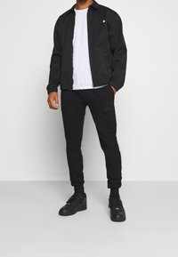 Svart lättviktsjacka med en skarp krage, ihop med svarta sweatpants med en minimalistisk design. Svarta sneakers fulländar outfiten.