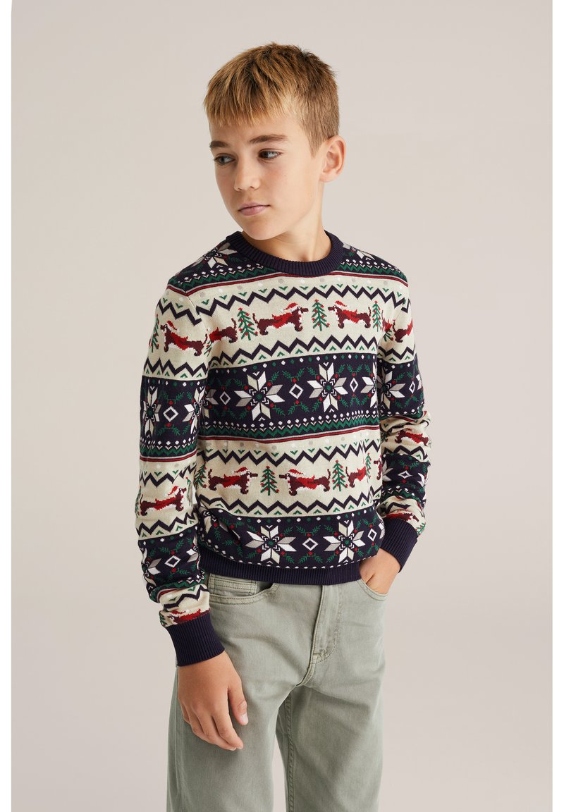 Stickad tröja med krämfärgad bakgrund och marinblå detaljer; har jöliga mönster med röda rävar, gröna träd och vita snöflingor.