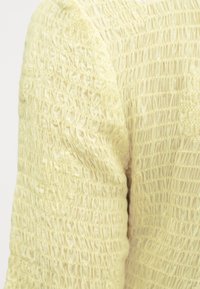 Κίτρινο υφασμάτινο με υφή που εμφανίζει ένα ζαρωμένο μοτίβο, με διακριτές οριζόντιες γραμμές που δημιουργούν μια στρωματοποιημένη εμφάνιση. Η επιφάνεια φαίνεται μαλακή.