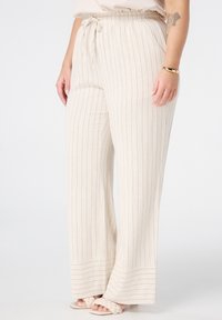 Helle beige weite Hose mit blauen Nadelstreifen, ausgestattet mit einem Kordelzugbund und einem weichTexturierten Stoff. Tragen mit hellen Sandalen.