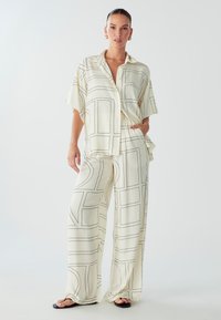 Crème blouse en wijde broek met zwart geometrisch lijnpatroon. Lichtgewicht stof, losse pasvorm en knoopsluiting op het shirt.