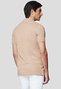Beżowa koszulka polo wykonana z miękkiego materiału, z krótkimi rękawami, prostym dołem i bocznymi rozcięciami dla wygody ruchów.