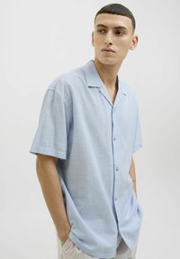 Camisa de manga corta en un suave tejido texturizado de color azul claro, con botones en el frente y un cuello clásico, que presenta un corte relajado.