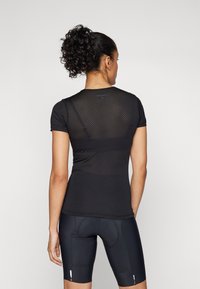 Svart kortermet treningstopp med mesh bak, designet for å gi god ventilasjon, sammen med tettsittende svarte sykkelshorts for aktiv bruk.