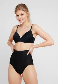 Juoda belaidė liemenėlė su lygiu, matinio paviršiaus audiniu ir gilia iškirpte, derinama su juodomis aukšto liemens formuojančiomis kelnaitėmis, abi be siūlių.