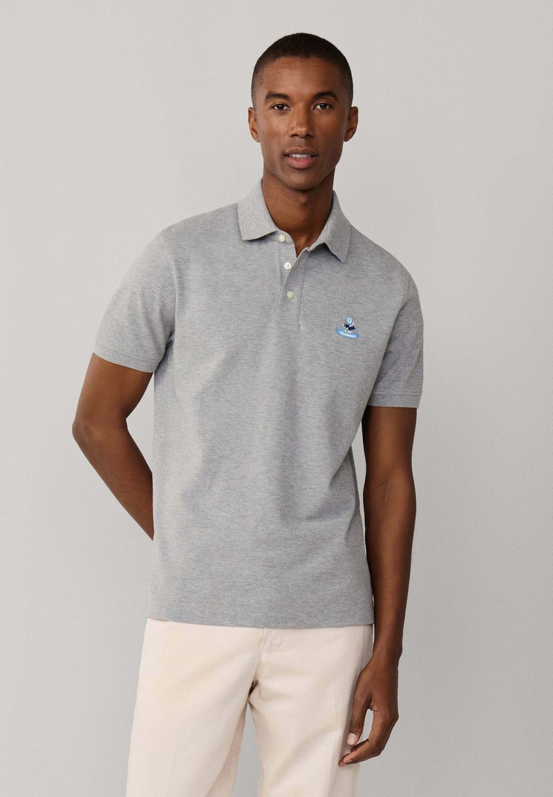Polo gris à manches courtes avec une patte de boutonnage à trois boutons et un petit logo brodé bleu sur la poitrine. Texture douce et coupe cintrée.
