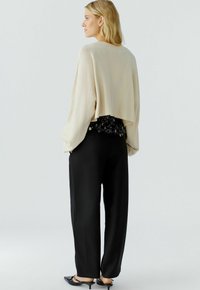 Beige cropped sweater over a floral black blouse, paired with black wide-leg trousers and pointed black shoes, viewed from the back.