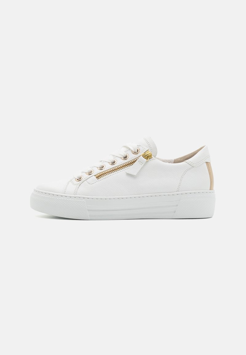 Basket basse blanche avec fermeture éclair dorée, lacets blancs, languette de talon beige et semelle en caoutchouc épaisse sur fond uni.