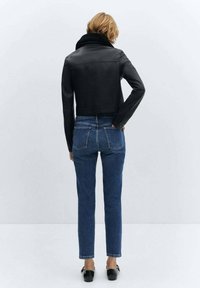 Veste courte en cuir noir avec un col montant, associée à un jean bleu taille haute, vue de dos. Texture lisse, coupe ajustée.