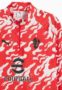 Rood gestippeld voetbalshirt met witte vlamontwerpen, een hoge kraag, een halve rits en een zwart Puma-logo met merktekst eronder.