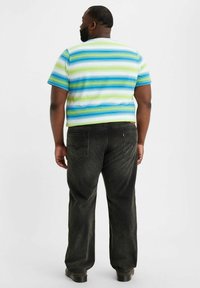 Randig kortärmad skjorta i blått, grönt och vitt; kombinerad med mörka, löst sittande jeans; synlig logo på bakfickan.