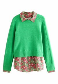 Maglione verde in lana con orlo e polsini a costine, indossato sopra una camicia a fantasia floreale con fiori rossi e verdi e colletto.