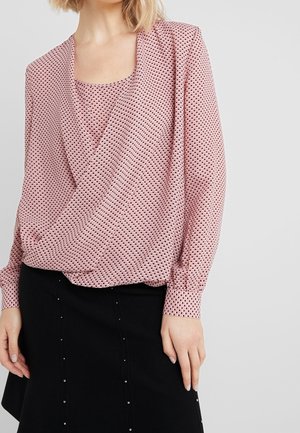 Donna che indossa una blusa rosa a maniche lunghe con pois neri e una gonna nera con piccole borchie decorative.