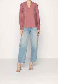 Blusa a maniche lunghe rosa polveroso con scollatura a V e colletto arricciato abbinata a jeans light blue a gamba dritta e tacchi a strisce bianche e nere.