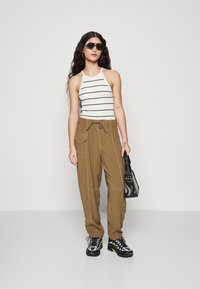 Hvit og svart stripete halterneck-top, brune bukser med elastisk midje og sidelommer, svart håndbag, svarte joggesko med gule detaljer.