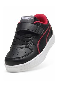 Zapatilla de cuero negra con superficie texturizada, detalles rojos, suela blanca y una combinación de cordones y una correa de velcro para el cierre.