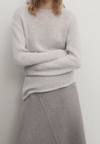 Pull gris clair tricoté avec une coupe ample, un col rond et des poignets côtelés, associé à une jupe grise douce avec un design asymétrique.