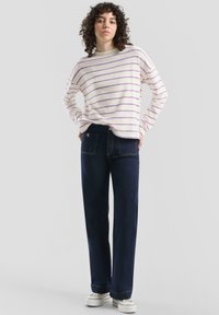 Biały sweter w paski z fioletowymi liniami, zestawiony z ciemnoniebieskimi szerokimi jeansami i białymi trampkami, prezentowany na neutralnym tle.