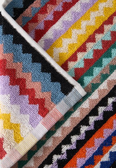 Έντονο υφαντό ύφασμα με ζιγκ-ζαγκ μοτίβο και διπλωμένη γωνία, με νήματα σε κόκκινο, κίτρινο, μπλε, μαύρο, μοβ και πράσινο χρώμα.