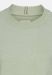 Lichtgroene gebreide pullover met een geribbelde kraag. Beschikt over een korte verticale rits in het midden en een textuur met subtiele variaties.
