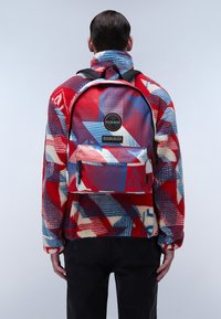 Mochila multicolor con patrones geométricos en rojo, azul y blanco. Fabricada en material sintético con correas ajustables negras.