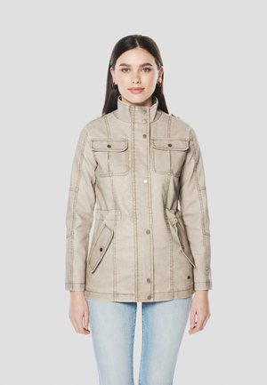 Világos bézs dzseki magas gallérral, négy első zsebbel és kontrasztos varrással. Az anyaga sima, szabott fazonú.