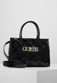 Sac à main en cuir verni noir avec motifs floraux en relief, logo argenté, poignées supérieures et une bandoulière amovible.