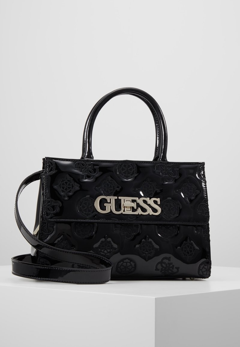 Sac à main en cuir verni noir avec motifs floraux en relief, logo argenté, poignées supérieures et une bandoulière amovible.