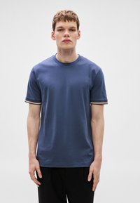 Kék rövid ujjú póló kontrasztos csíkos díszítéssel a mandzsettákon, kerek nyakkivágással, puha pamut anyagból, testhez simuló szabással.